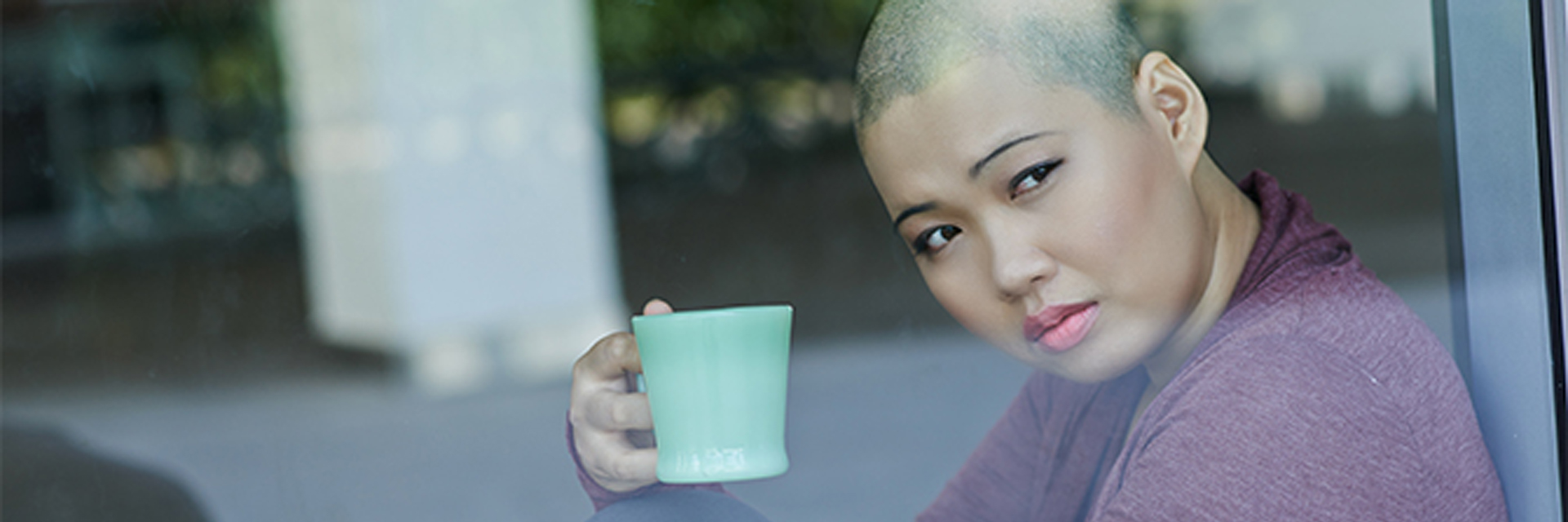 Woman starting out window with coffee mug in her hand