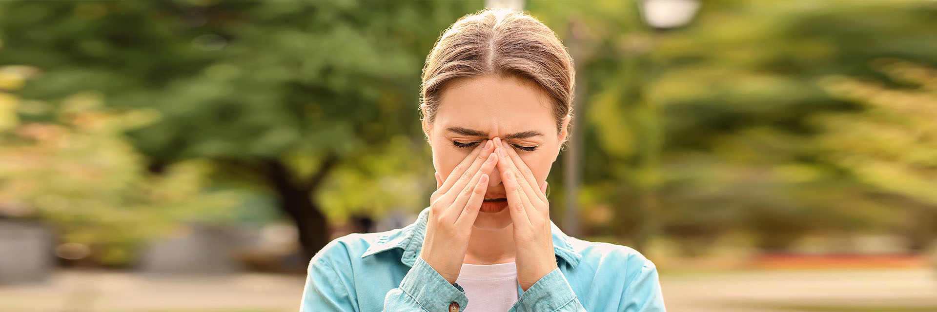 Woman holding her head while outdoors suffering from allergies